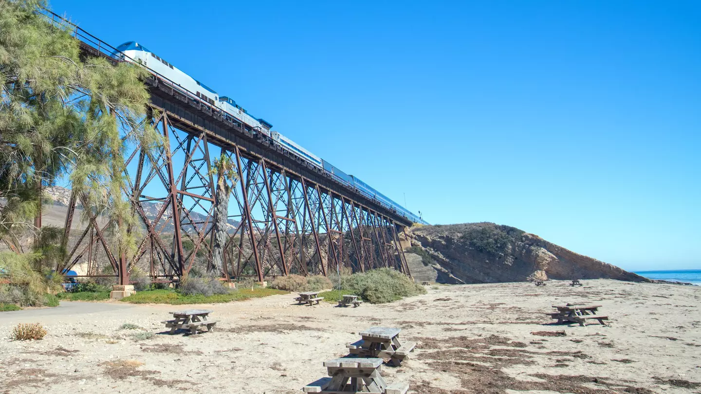 Train traveling over a railroad track bridge that rises high above a beach