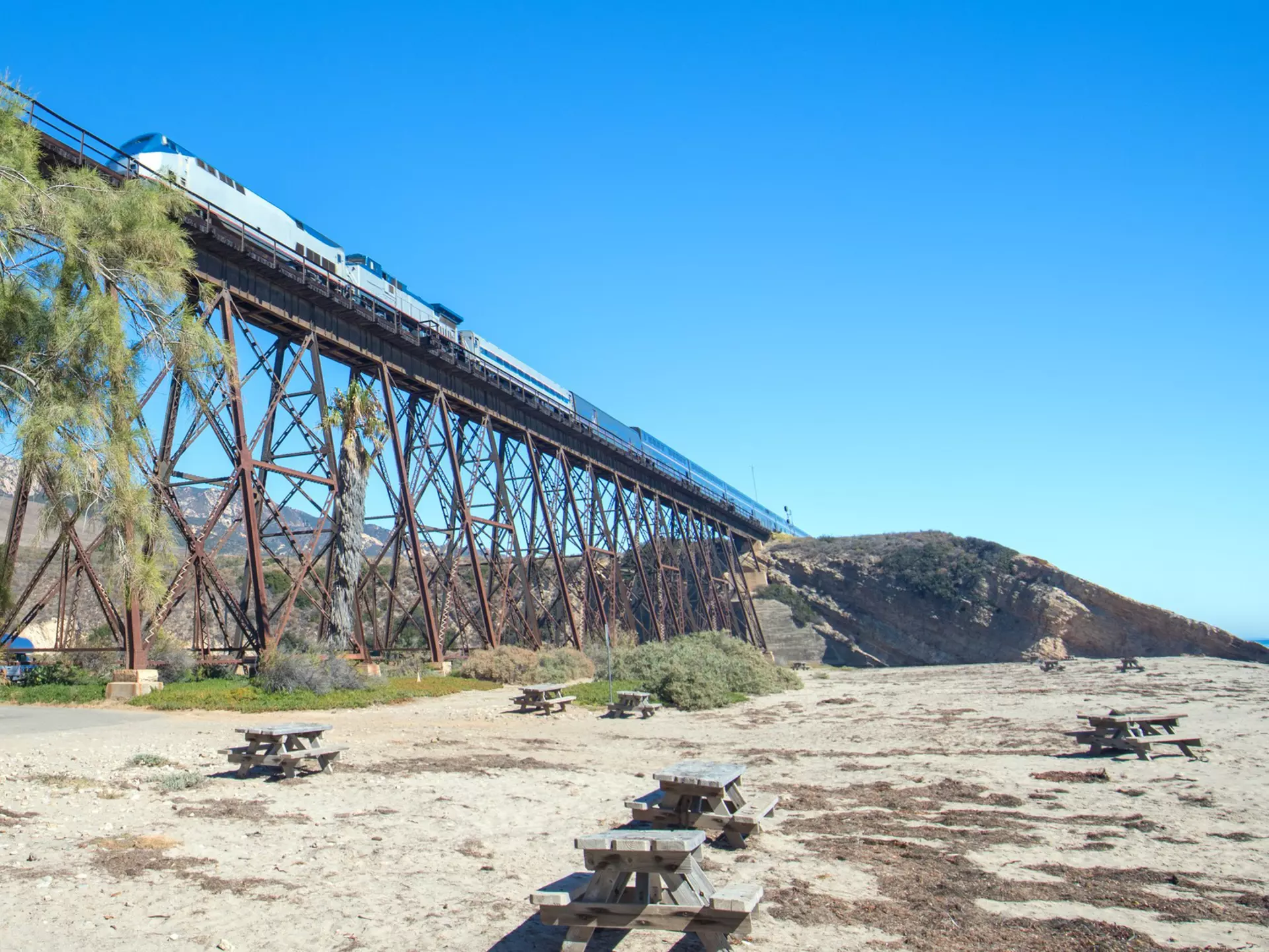Train traveling over a railroad track bridge that rises high above a beach