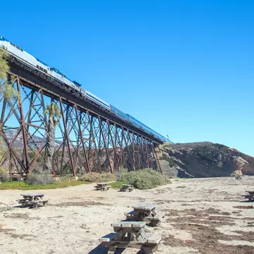 Train traveling over a railroad track bridge that rises high above a beach