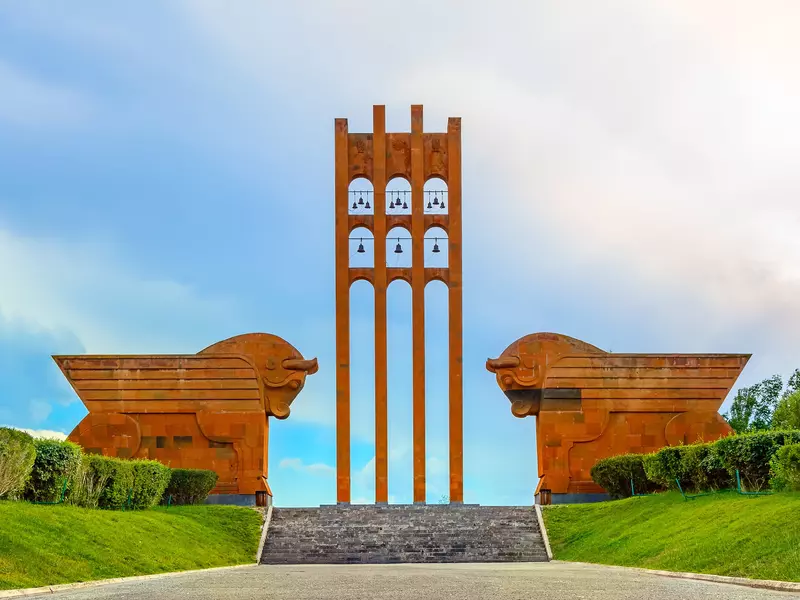 Two large orange bulls flank the staired entrance of a memorial that has an orange tower with bells