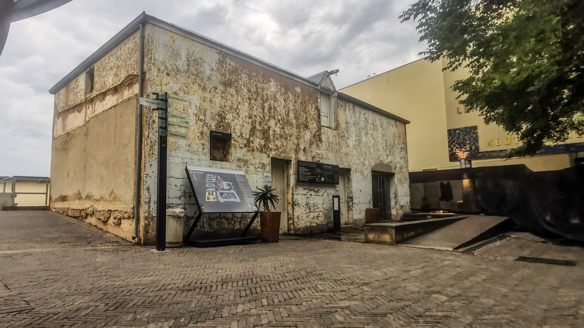 Weathered old building with peeling plaster, wayfinding signs and a site map on a brick-paved courtyard