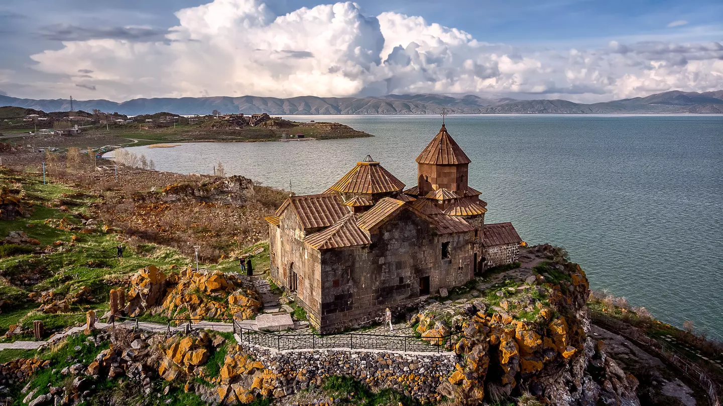 Dramatic clouds rise behind Hayravank Monastery on the shores of Lake Sevan, Armenia.