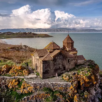 Dramatic clouds rise behind Hayravank Monastery on the shores of Lake Sevan, Armenia.