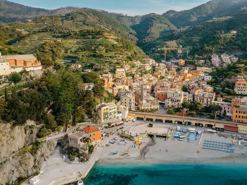 Aerial view of a classic clifftop town with colorful buildings, vinetards and field overlooking a beach and port