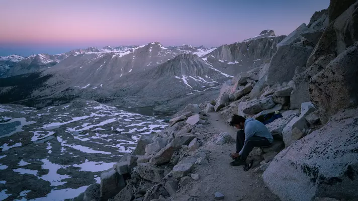 A hiker pauses on the final stretch of a trail to adjust his footwear.