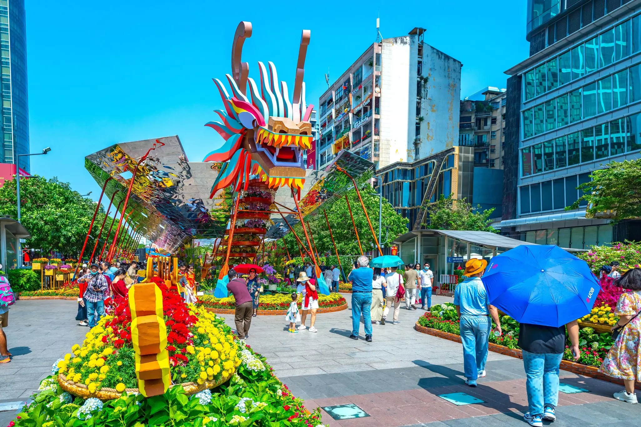 A pedestrian street lined in flower beds overlooked by a large dragon installation