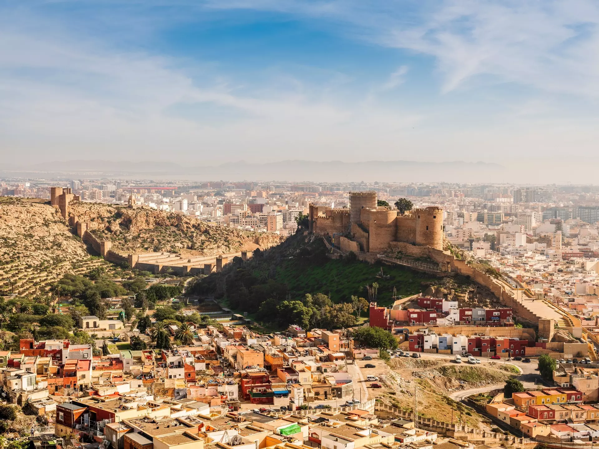 A vast ancient fortress citadel on a hill above a coastal town.