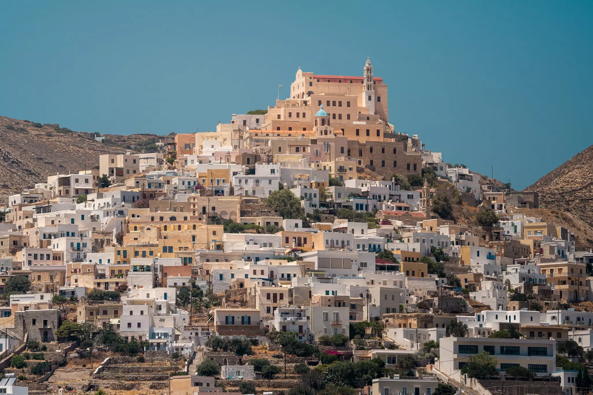 A town in the Cyclades, Greece, is built on a hillside, leading up to an imposing church at the top.