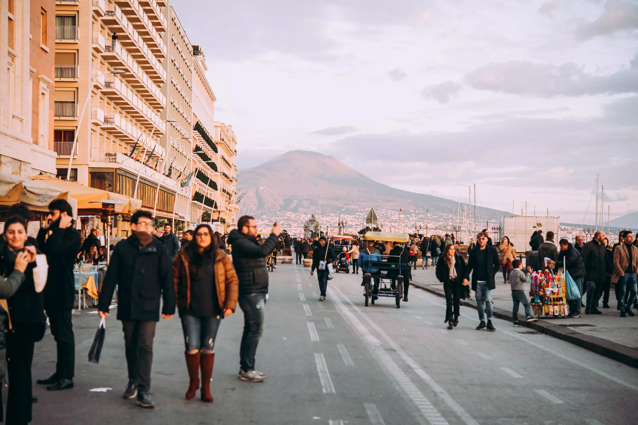 Naples in winter with people wandering along a road by the seaside in winter clothes on