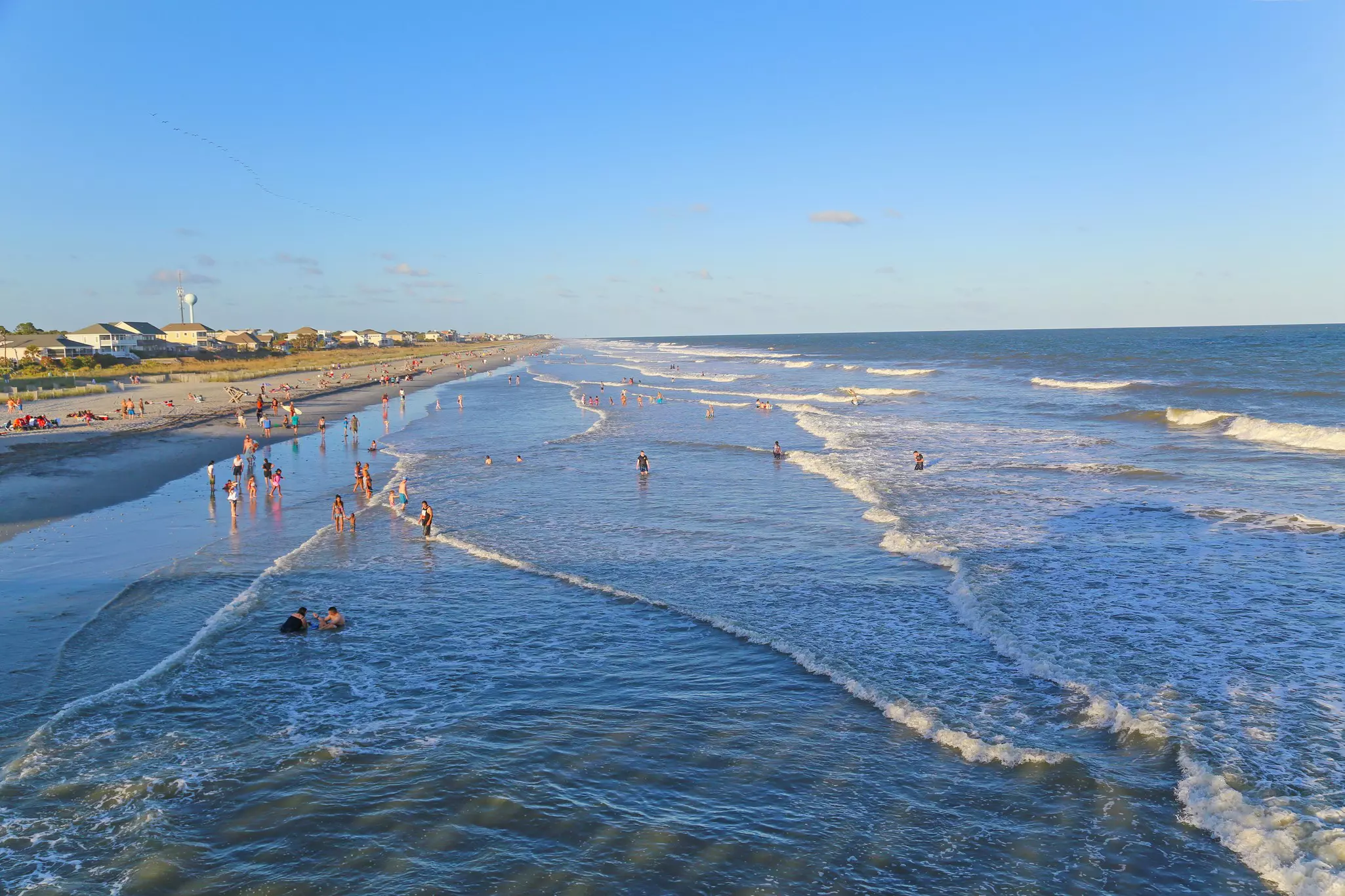 People paddling in the water at Folly Beach on a sunny day.