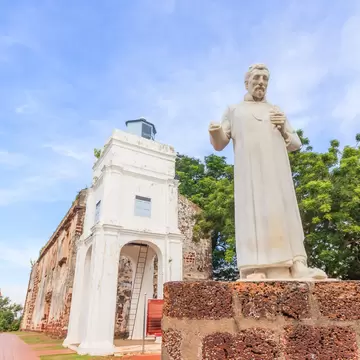 White bell tower and weathered laterite walls of St Paul's Church on a hilltop in Melaka, with a marble saint statue