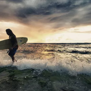 Surfer exiting water with surfboard at sunset in Rincon, Puerto Rico