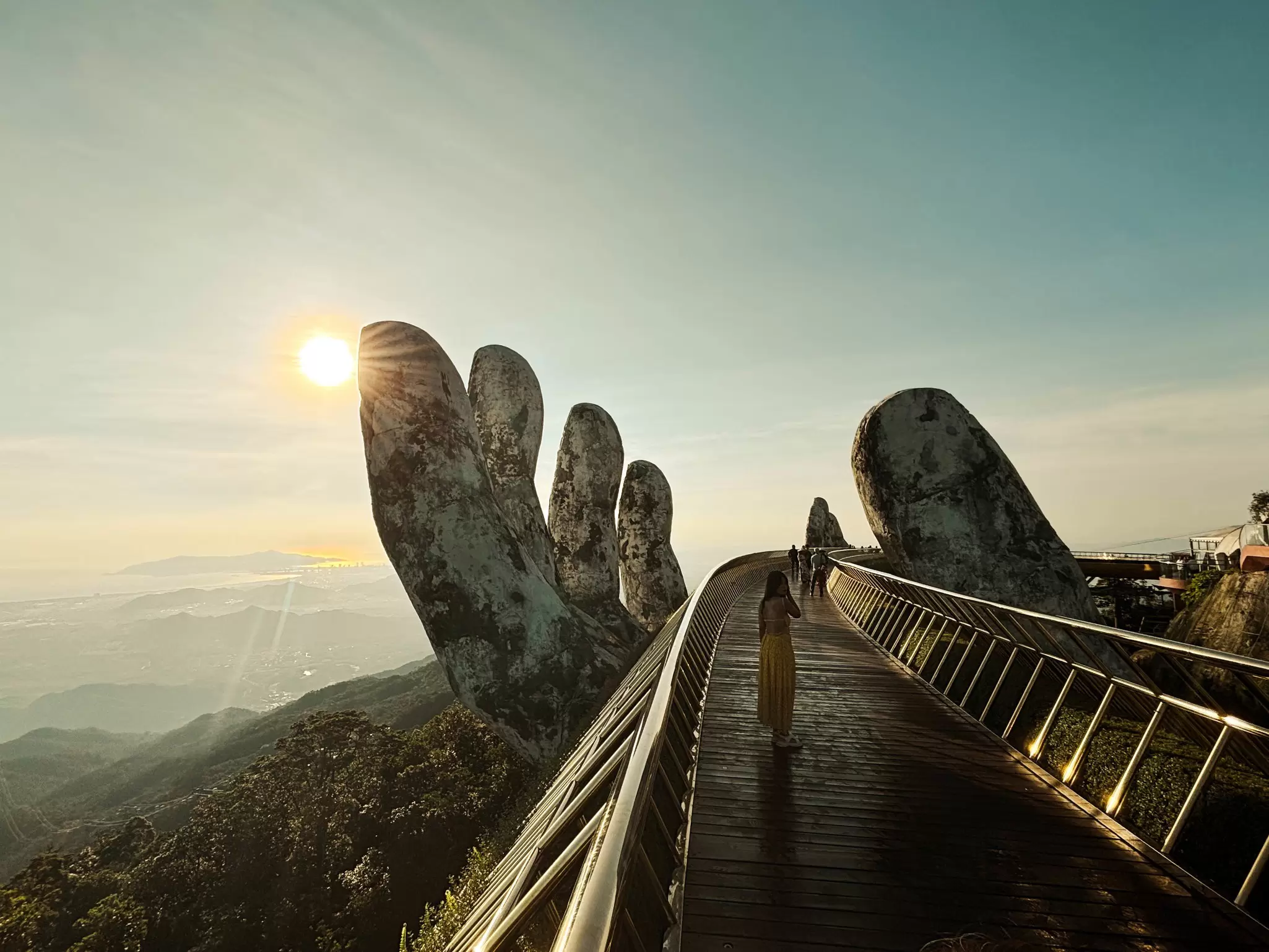 People walk in the early morning on a bridge supported by a giant carved human hand, Danang, Vietnam