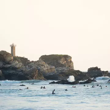 Evening light paints the lighthouse of Punta Zicatela, while many surfers pack the lineup in Puerto Escondido, Mexico