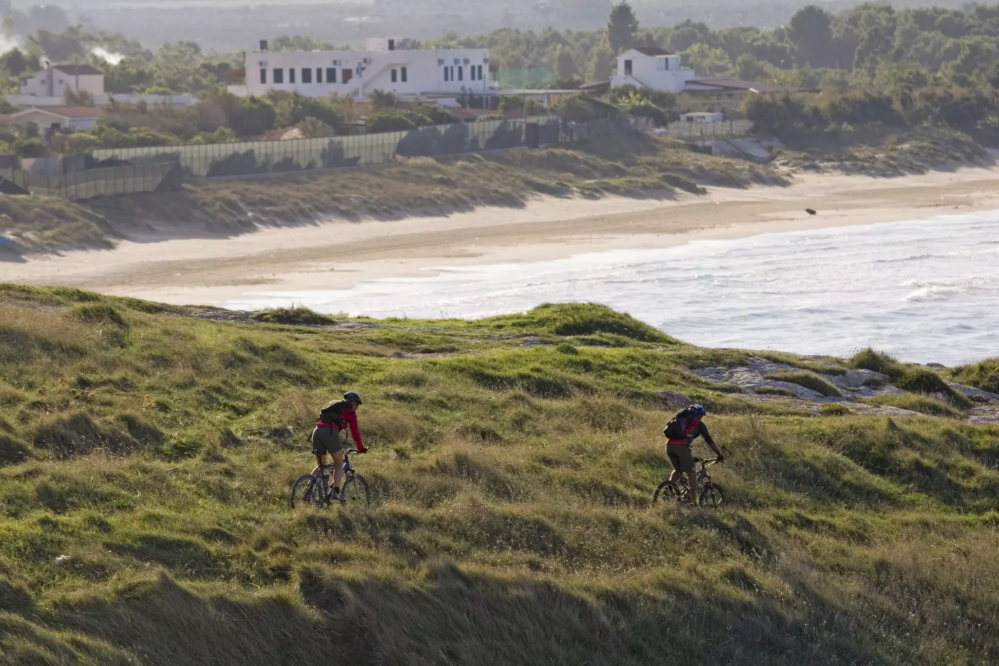 Two mountain-bike cyclists follow a trail on a coastal bluff.