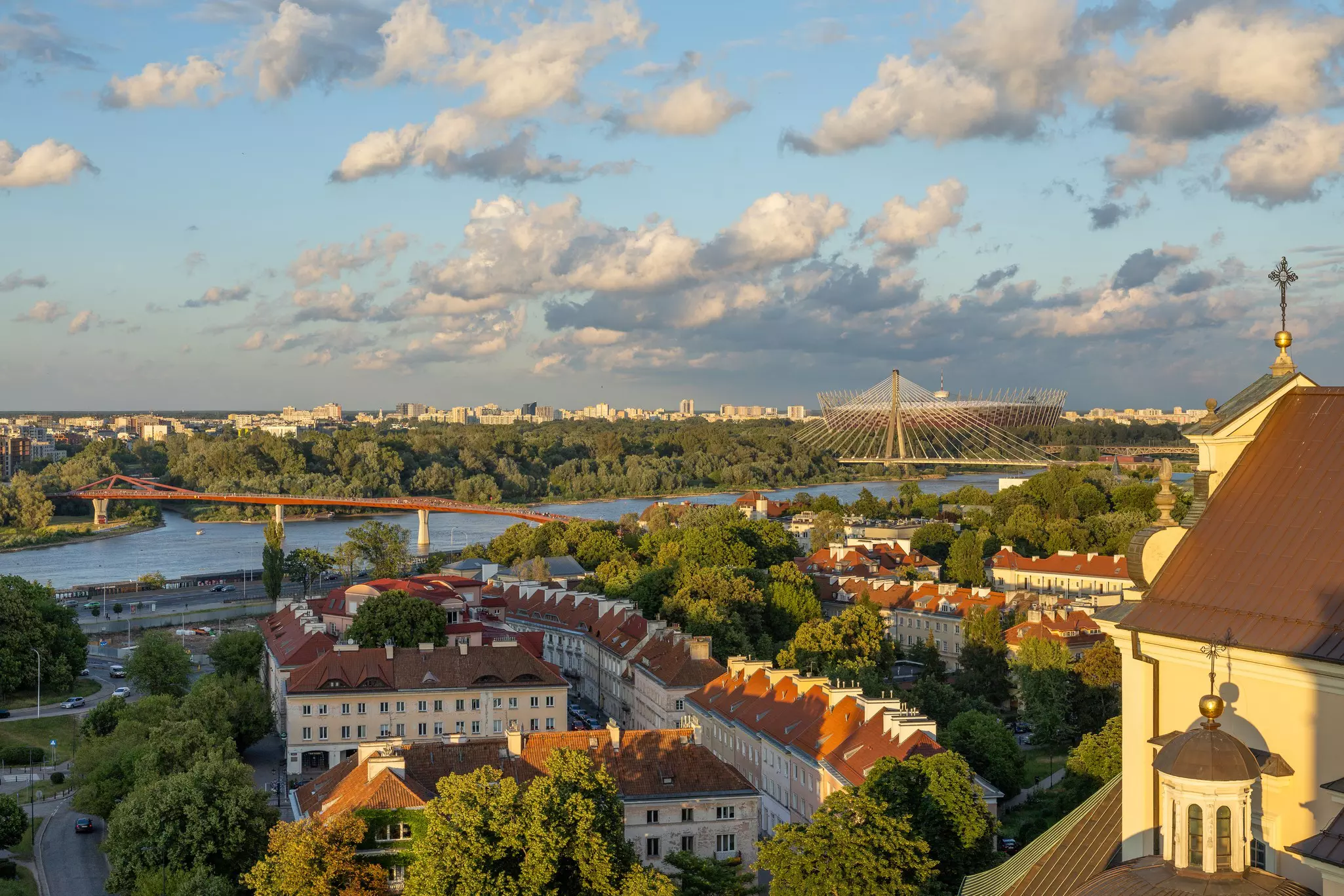The river, bridges and buildings of Warsaw, Poland, in evening light under blue sky with white puffy clouds.