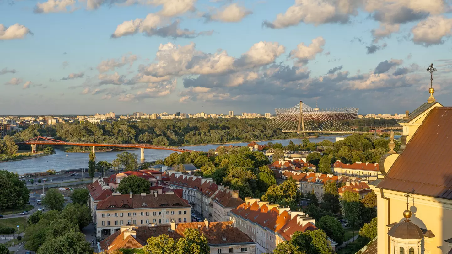 The river, bridges and buildings of Warsaw, Poland, in evening light under blue sky with white puffy clouds.