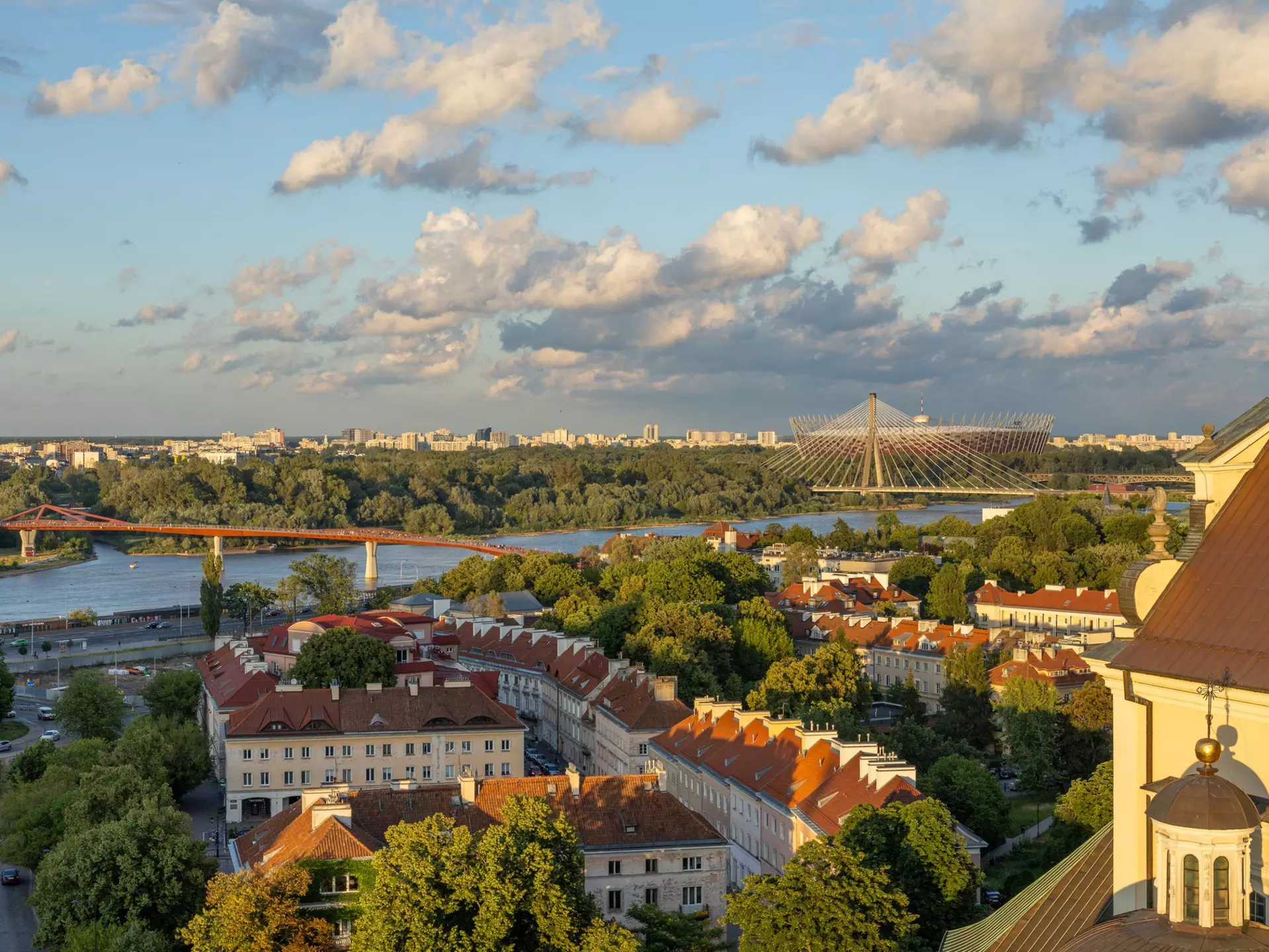 The river, bridges and buildings of Warsaw, Poland, in evening light under blue sky with white puffy clouds.