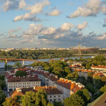 The river, bridges and buildings of Warsaw, Poland, in evening light under blue sky with white puffy clouds.