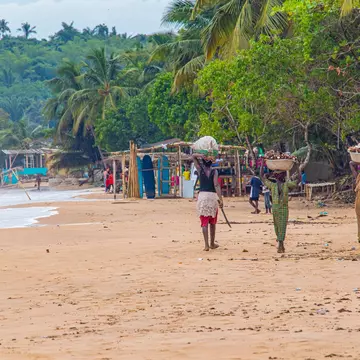 Busua, Ghana - May 10th, 2024: The people of Ghana. Local African women carrying basket while walking on the beach., License Type: media, Download Time: 2024-07-04T06:33:53.000Z, User: mvm_lonelyplanet, Editorial: true, purchase_order: 56530, job: Global Publishing-WIP, client: The World 3, other: Virginia Moreno