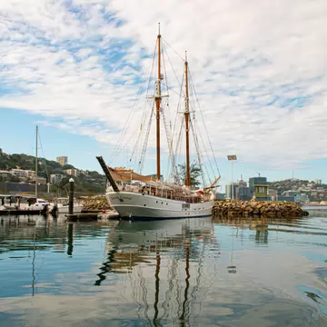 Two-masted schooner Joseph Conrad moored by a breakwater in Port Moresby, Papua New Guinea, with hillside homes behind