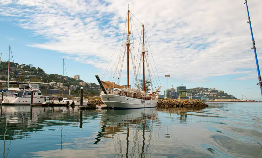 Two-masted schooner Joseph Conrad moored by a breakwater in Port Moresby, Papua New Guinea, with hillside homes behind