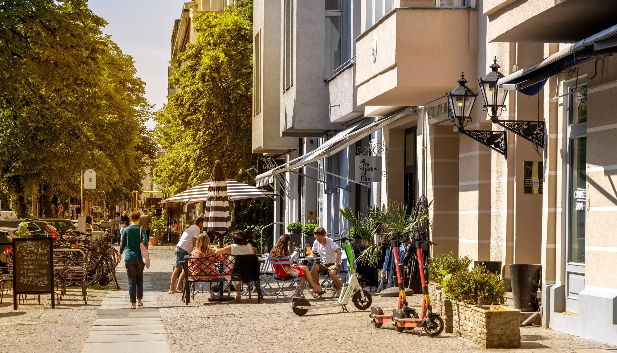 People sit at an outdoor table on a sidewalk in a city on a summer day.