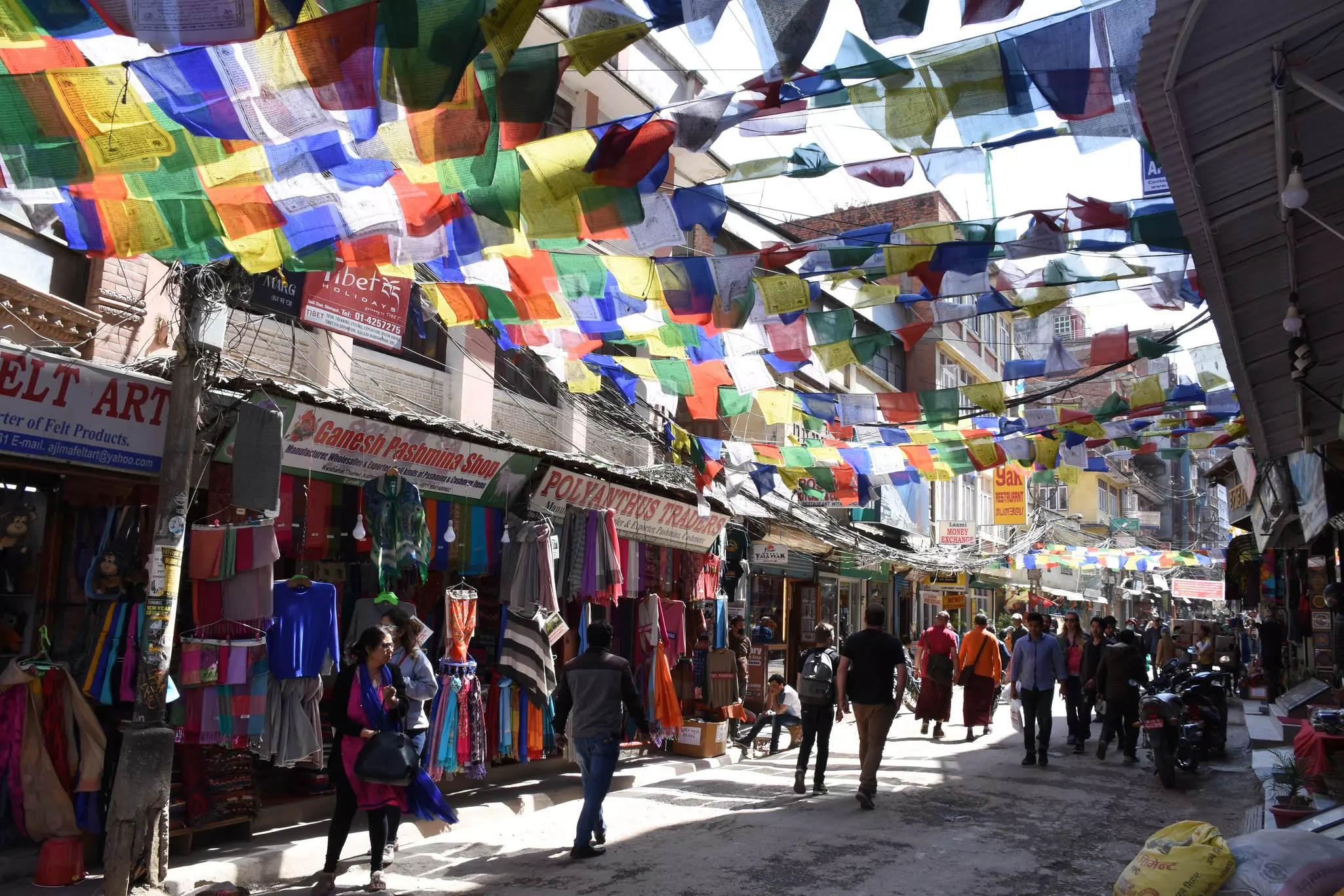 Colorful flags are strung across a plaza between storefronts that have their wares displayed outside