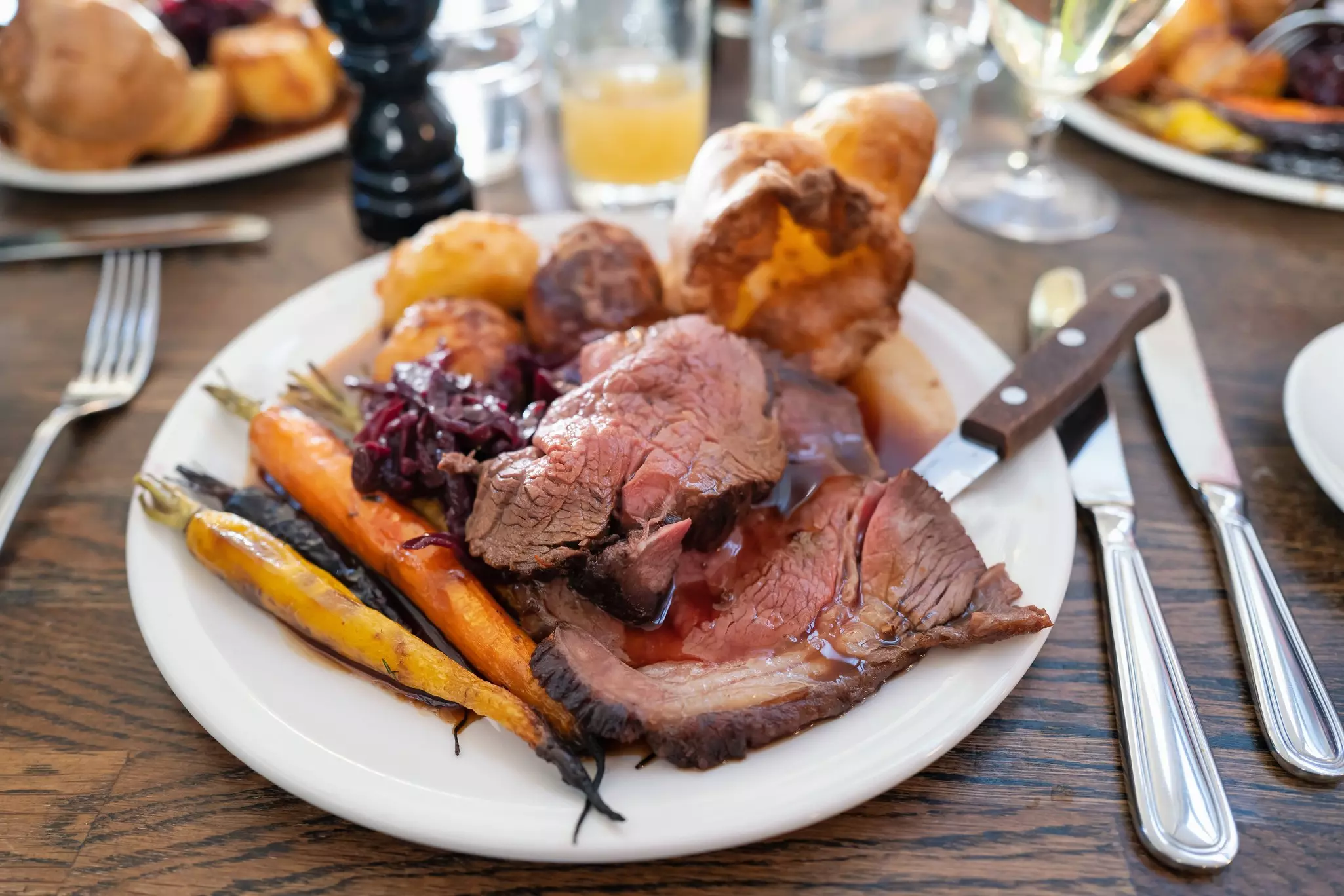 Roast beef on a white plate with roast potatoes and Yorkshire pudding with vegetables in a restaurant, England.
