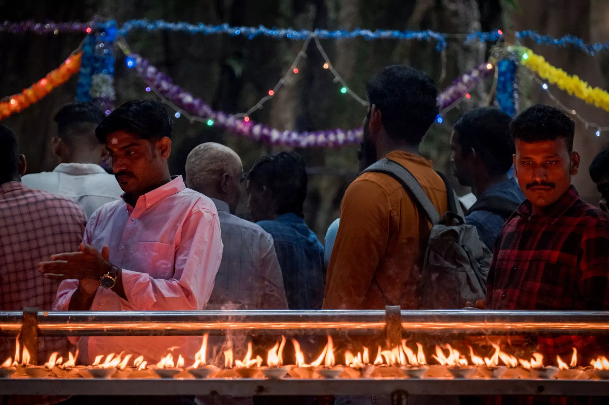 People at a temple pray as the walk by a shelf with burning lamps.
