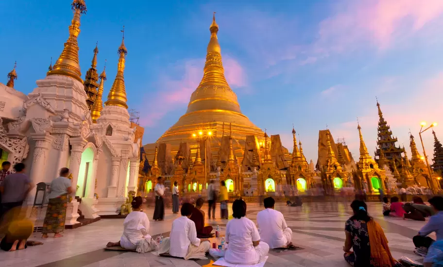 Worshippers in white sit on the marble terrace of Shwedagon Pagoda in Yangon, the gold stupa lit at dusk