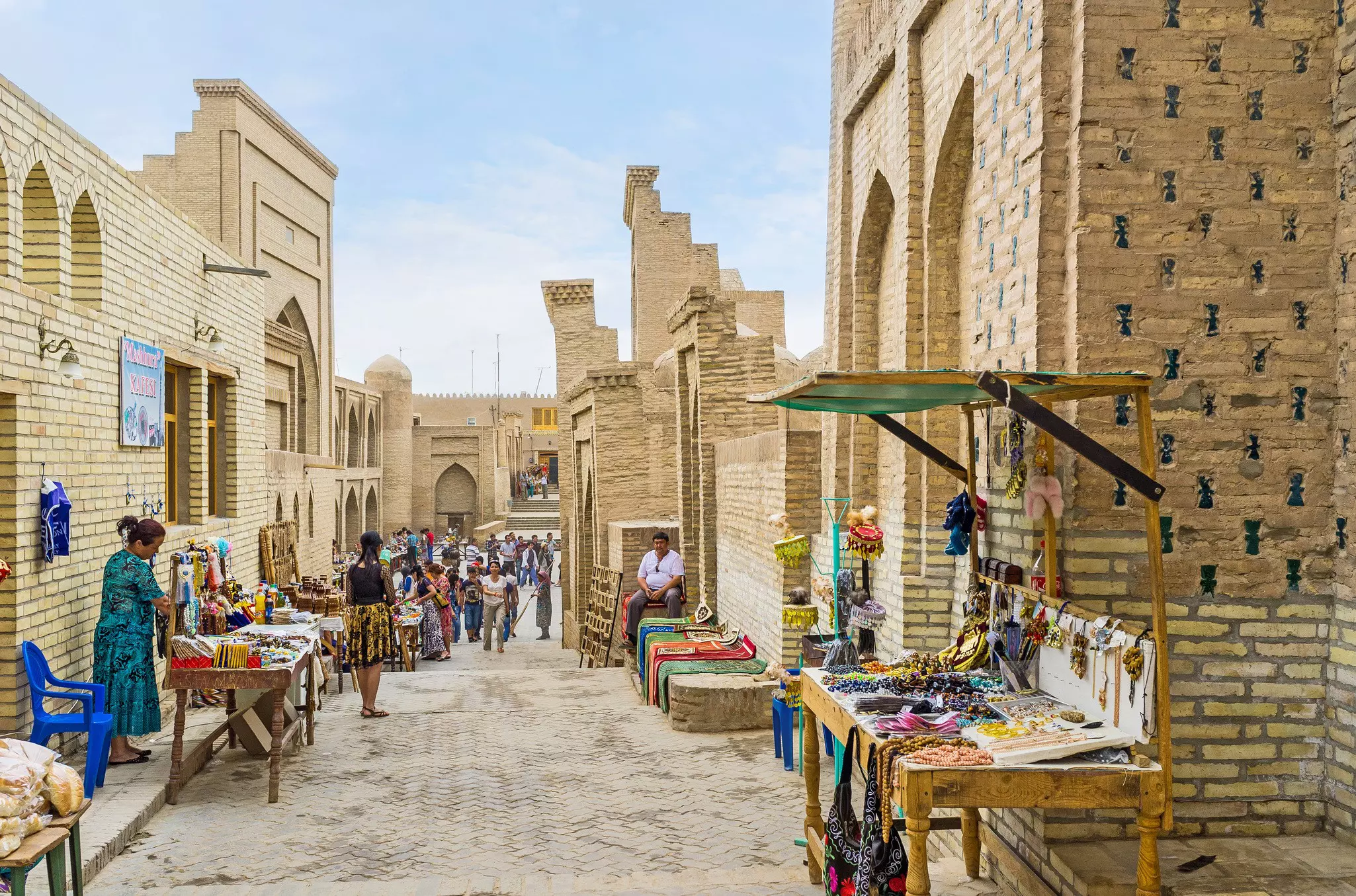 An alleyway between ancient walls lined with a series of market stalls and traders in Khiva, Uzbekistan