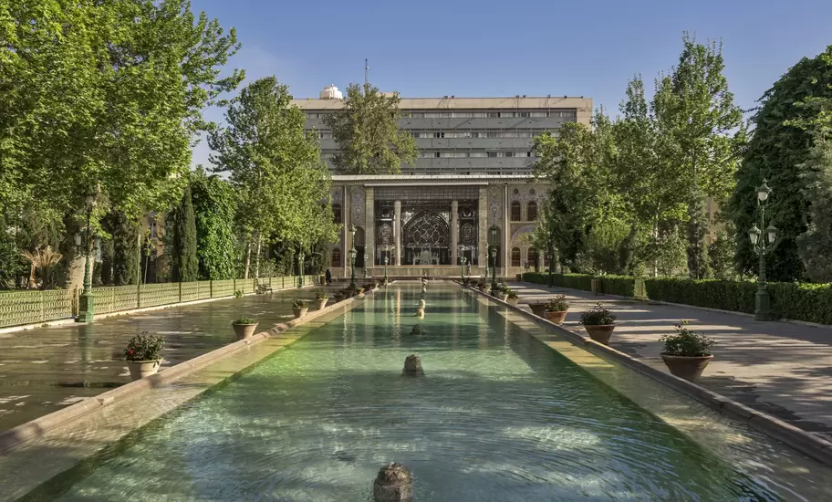 Long reflecting pool and fountains leading to the tiled, mirrored facade of Golestan Palace in Tehran, Iran, lined by trees