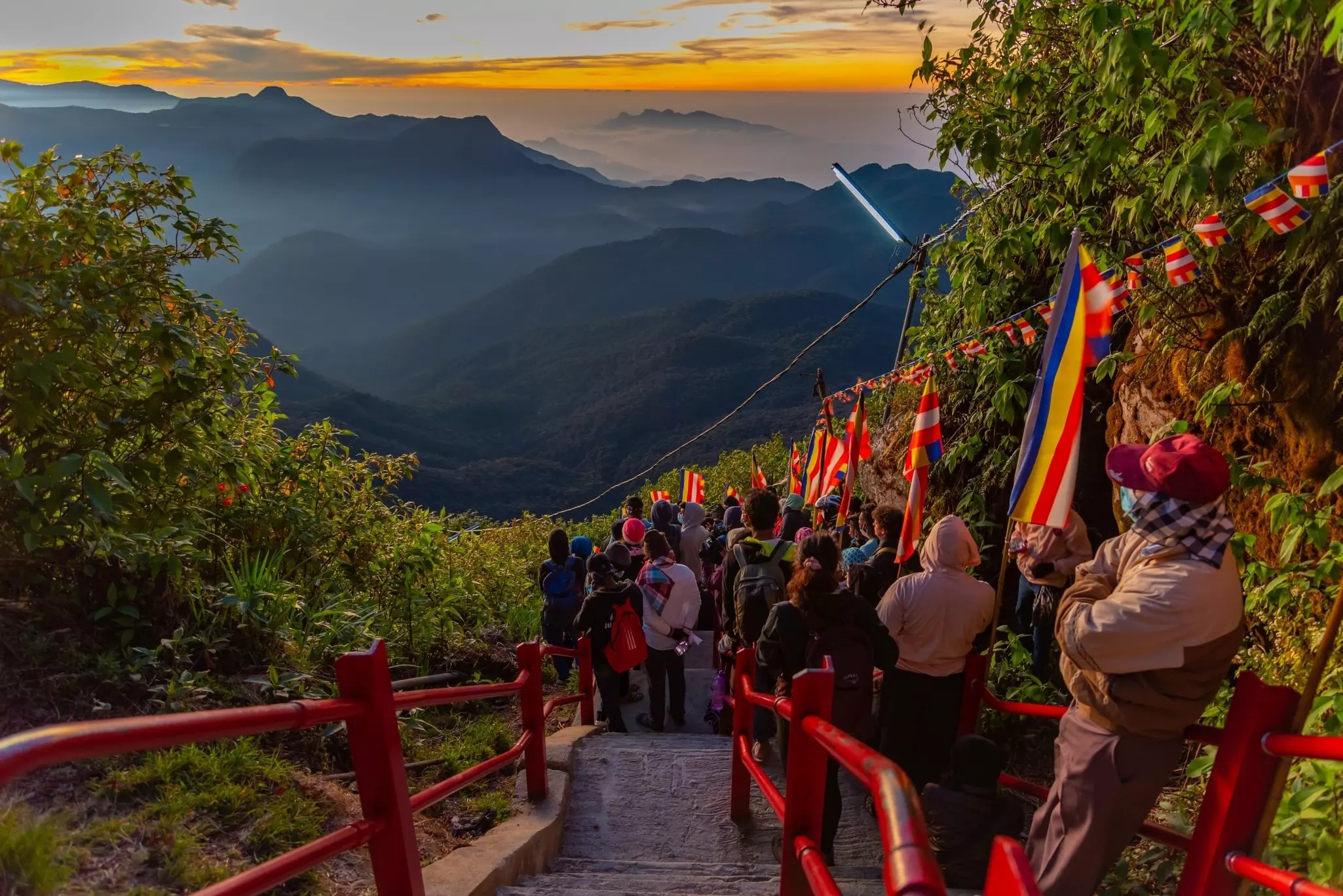 People stand on a series of steps lined with flags as the dawn breaks over distant hills.