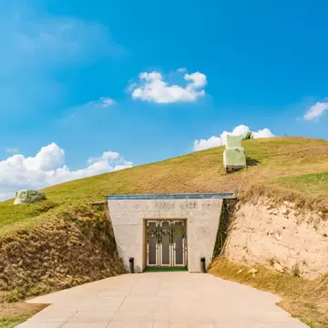 A stone doorway set into a grassy burial mound under a blue sky.