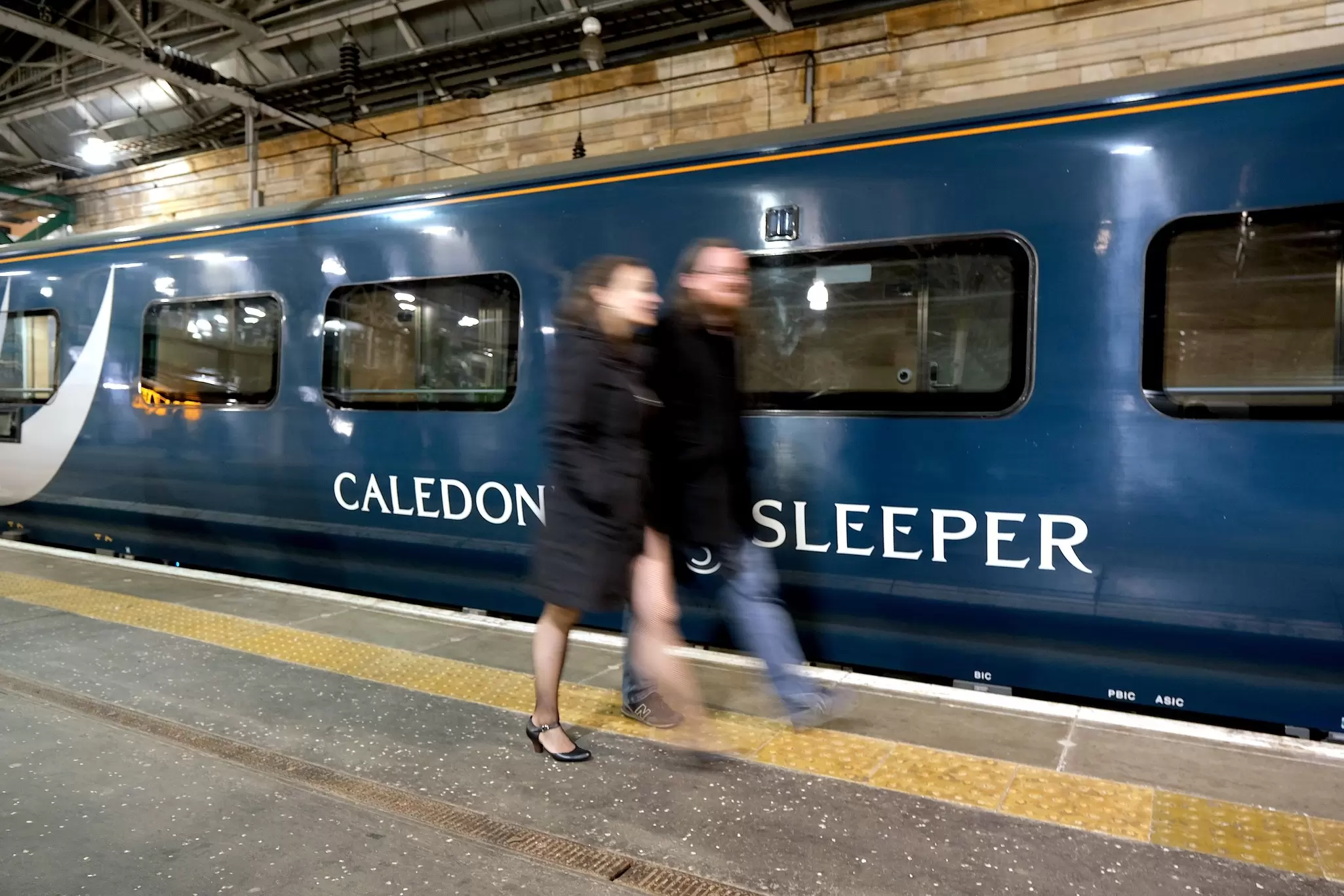 Edinburgh, Scotland - October 31 2019:A couple walk past the Caledonian Sleeper train in Waverley Station, Edinburgh, License Type: media, Download Time: 2025-12-10T17:24:14.000Z, User: rhylton_redventures, Editorial: true, purchase_order: 65050 - Digital Destinations and Articles, job: Lonely Planet , client: wip, other: Rhianydd hylton