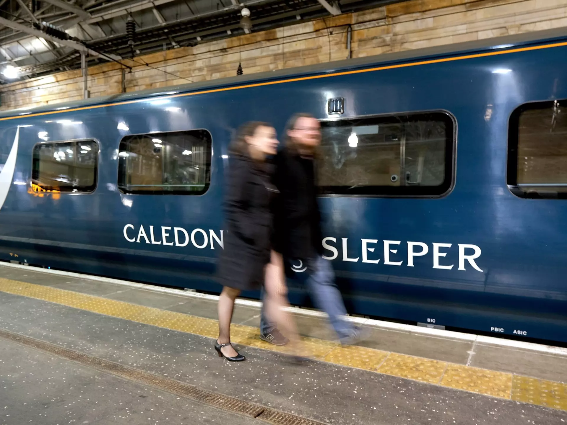 Edinburgh, Scotland - October 31 2019:A couple walk past the Caledonian Sleeper train in Waverley Station, Edinburgh, License Type: media, Download Time: 2025-12-10T17:24:14.000Z, User: rhylton_redventures, Editorial: true, purchase_order: 65050 - Digital Destinations and Articles, job: Lonely Planet , client: wip, other: Rhianydd hylton
