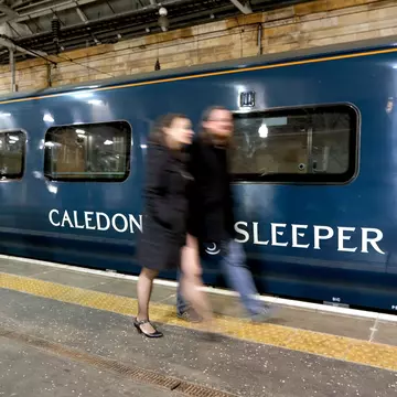 Edinburgh, Scotland - October 31 2019:A couple walk past the Caledonian Sleeper train in Waverley Station, Edinburgh, License Type: media, Download Time: 2025-12-10T17:24:14.000Z, User: rhylton_redventures, Editorial: true, purchase_order: 65050 - Digital Destinations and Articles, job: Lonely Planet , client: wip, other: Rhianydd hylton