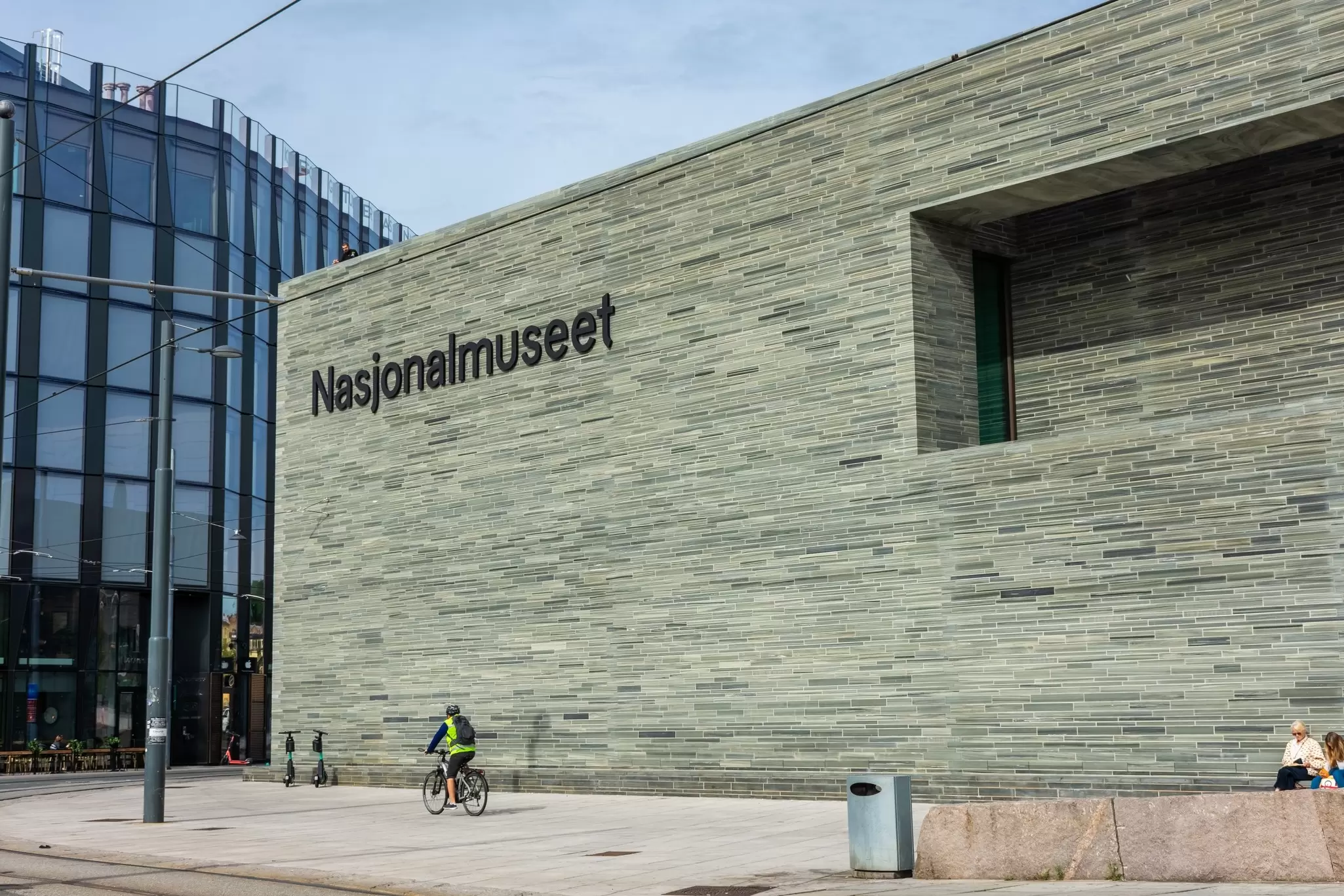 A cyclist rides near a large gray building with a sign that says Nasjonalmuseet: the National Museum in Oslo.