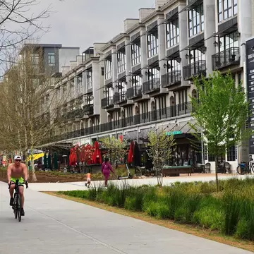 A cyclist pedals down a path next to trees and apartment complexes in a city.