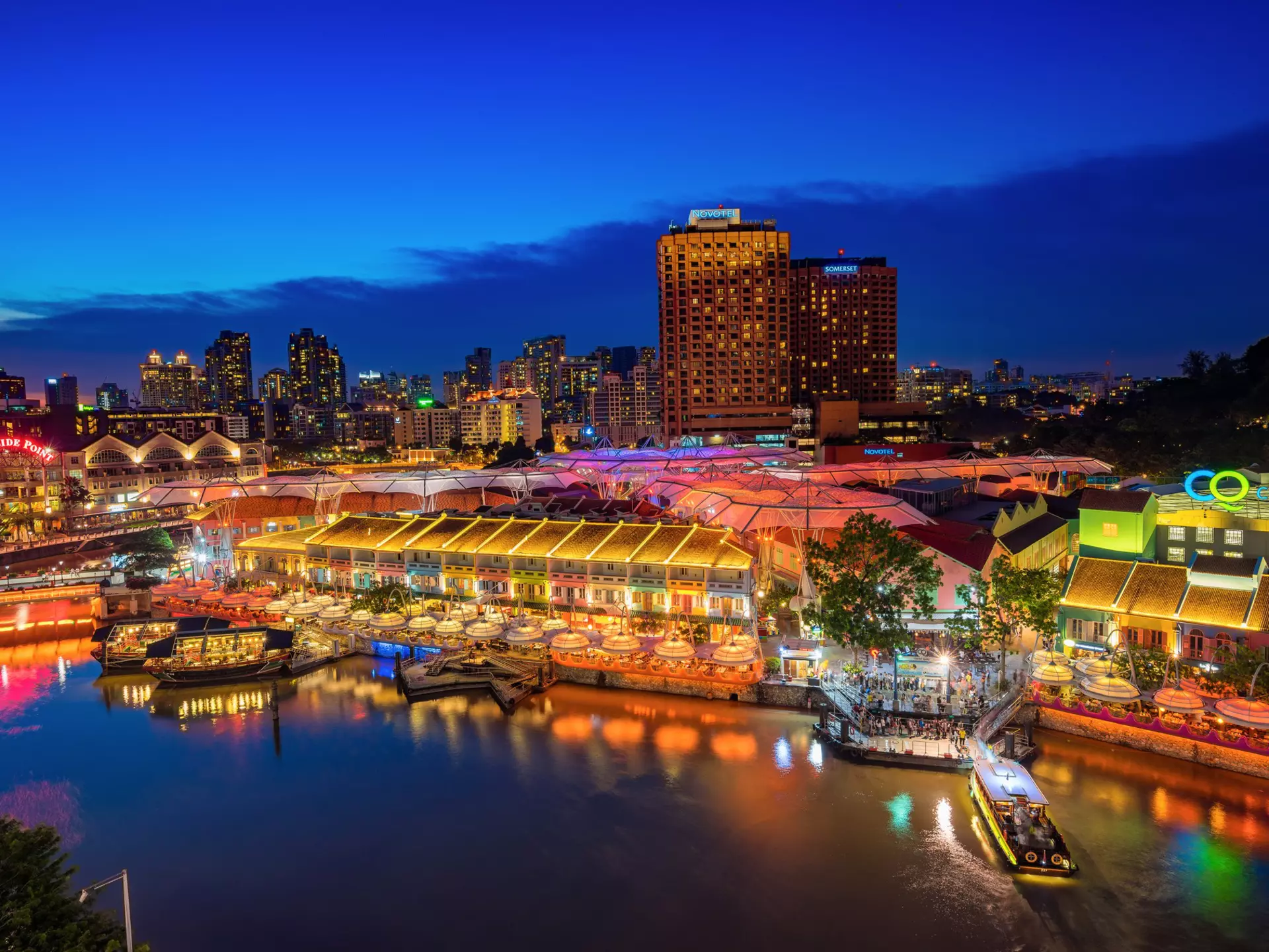 An evening scene of buildings colorfully lit by a river in a city.