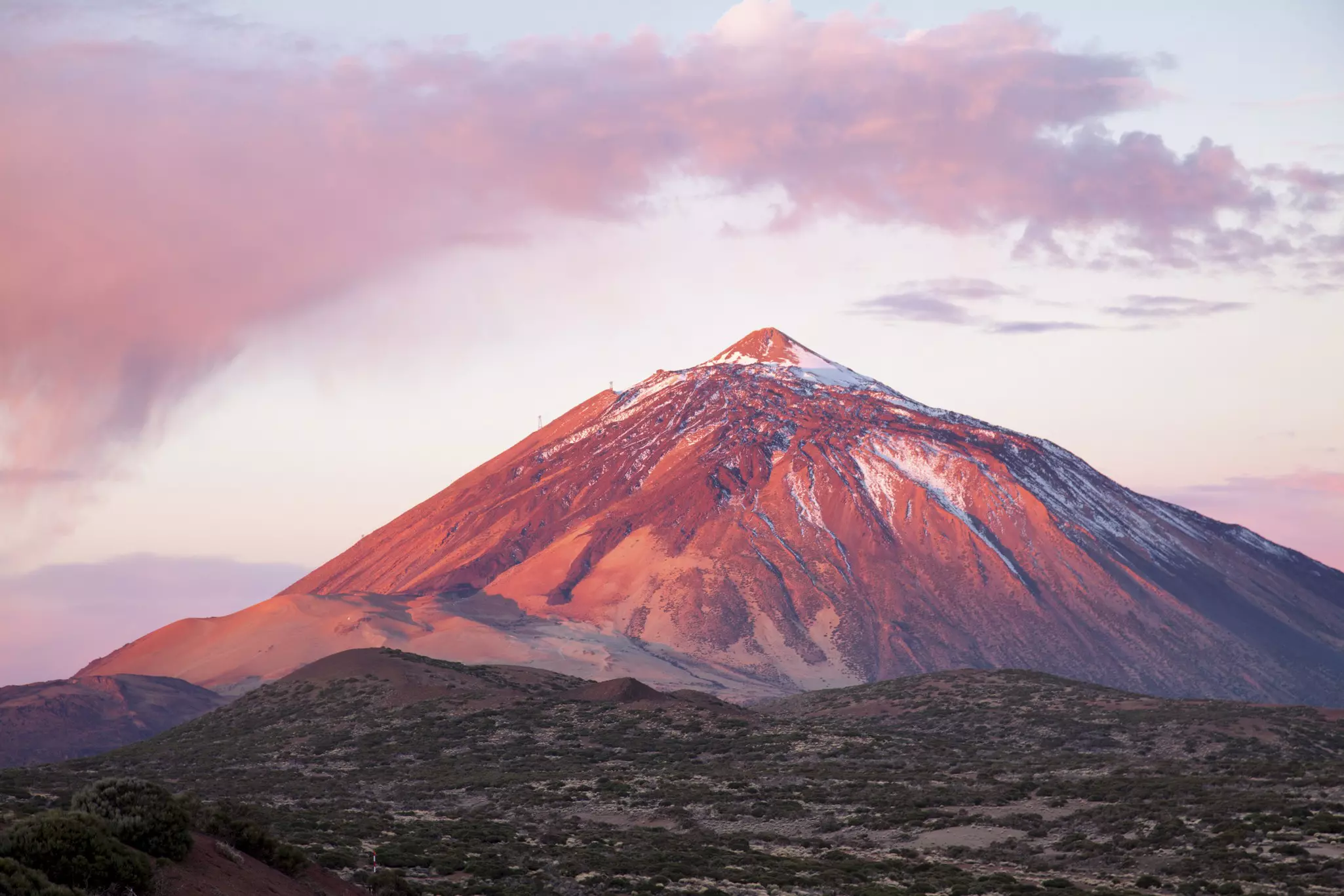 A view of a snow-dusted volanic peak in reddish sunset light
