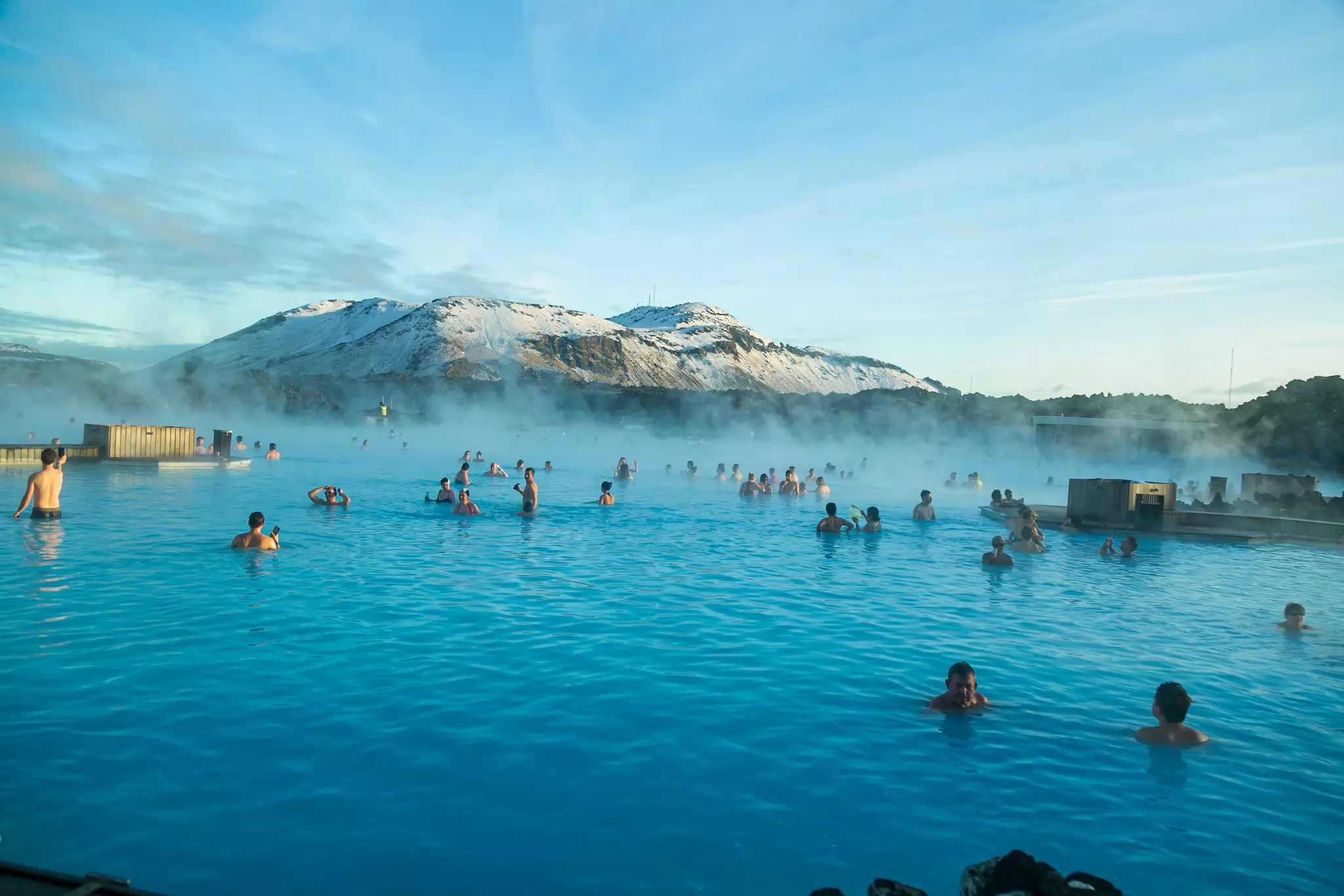 People bathing in a hot spring with a snowy mountain backdrop