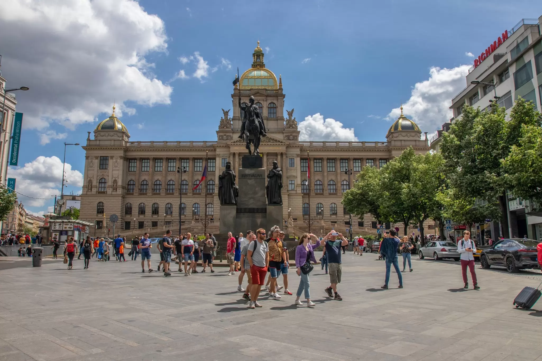 People walk around Wenceslas Square, with the statue of St Wenceslas and the National Museum in the background in Prague, Czechia.