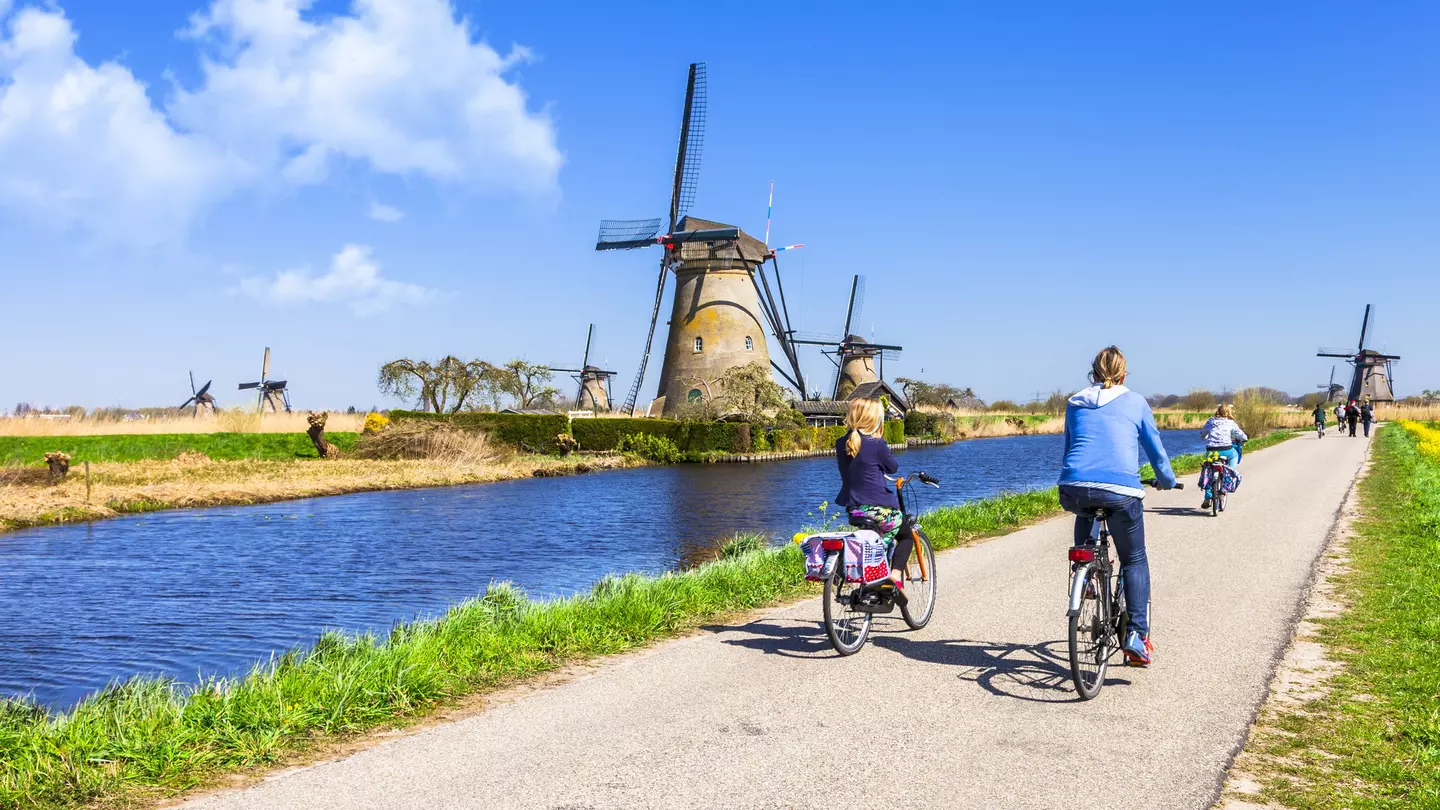 Mother and children ride bicyles on a path past windmills at Kinderdijk