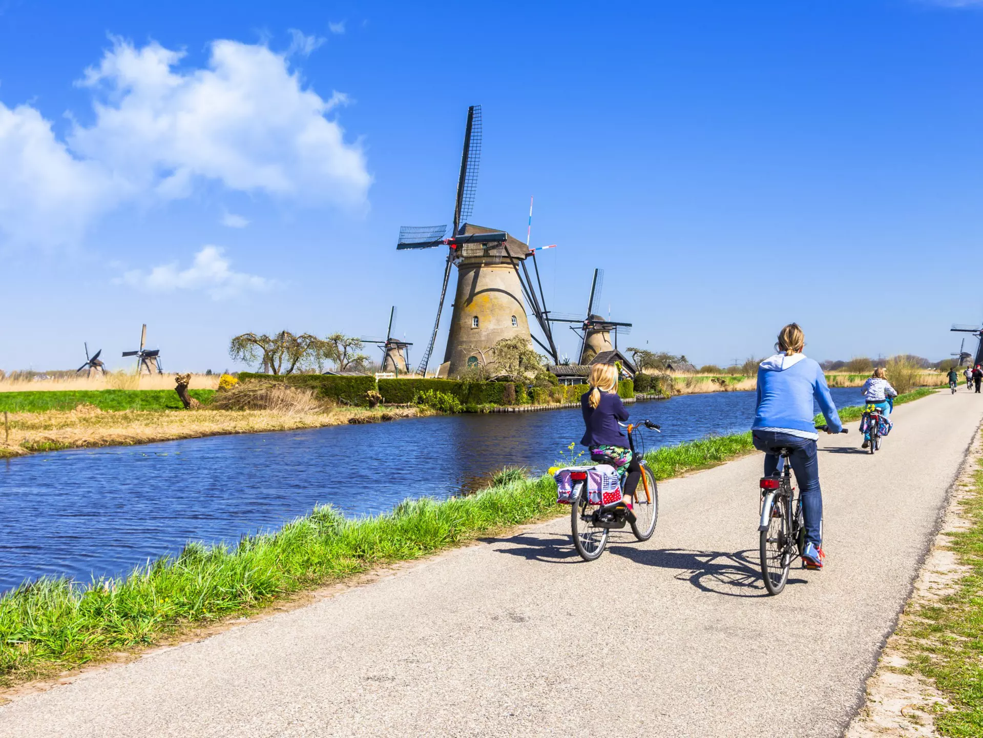 Mother and children ride bicyles on a path past windmills at Kinderdijk