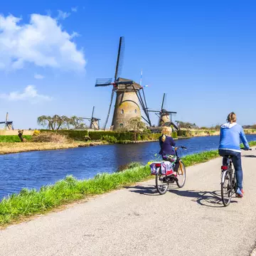 Mother and children ride bicyles on a path past windmills at Kinderdijk