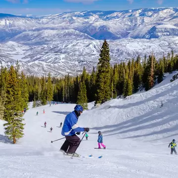 A skier on the slopes above snow-covered woodland and distant mountains: Aspen, Colorado