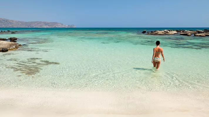 A woman walks into the turquoise water of the sea at the beach. 