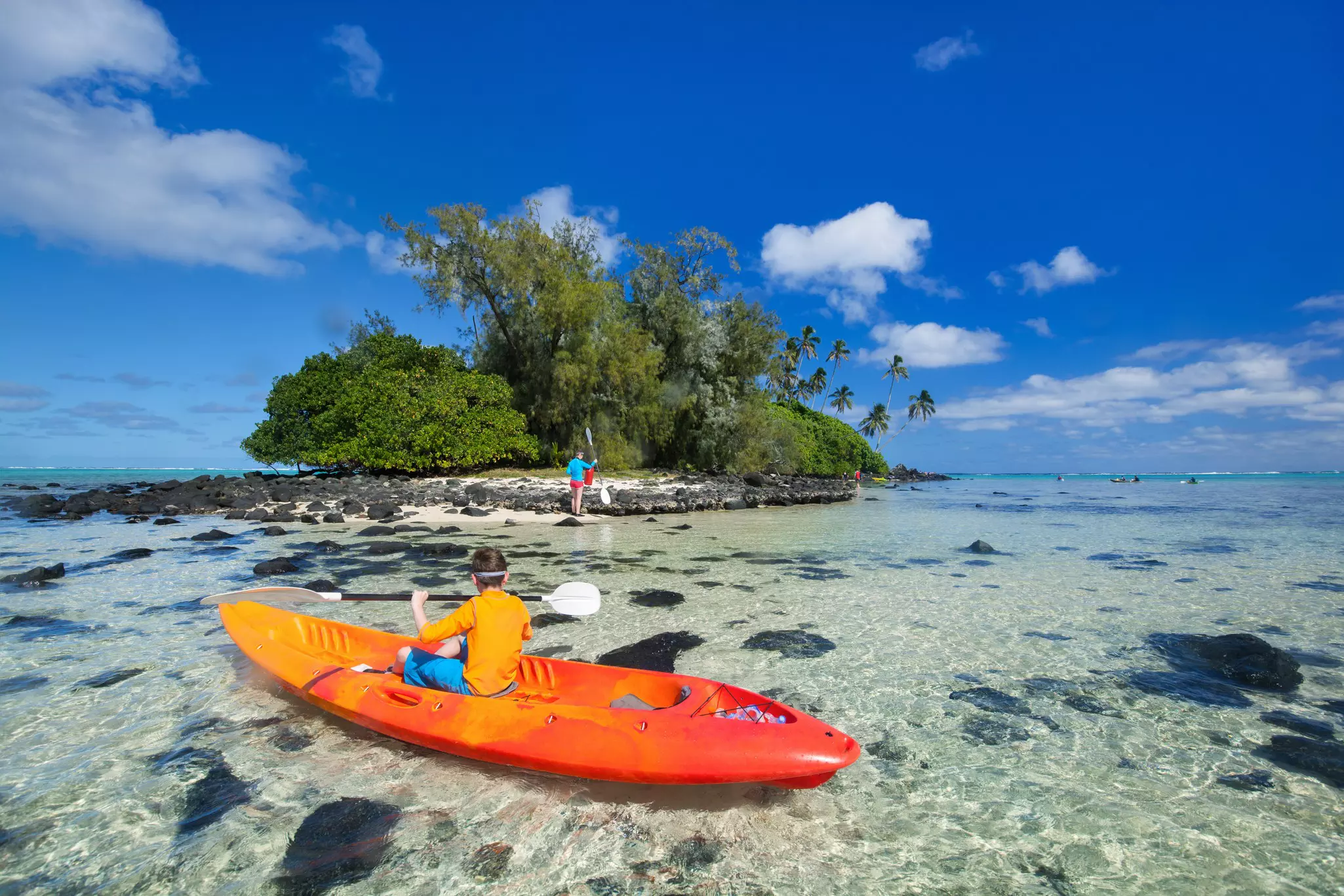 Teenage boy on a kayak on Muri Lagoon with another kayaker standing in the background
